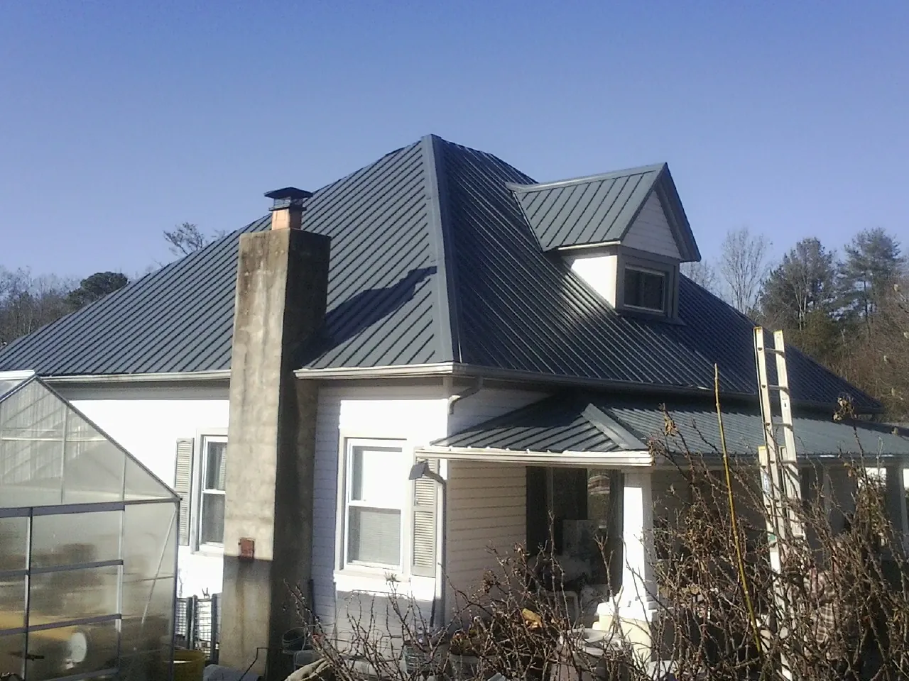 Dark blue standing seam metal roof on a white farmhouse with dormer — Slate & Tile Roof Repair by Roofing Brothers in Fall Branch