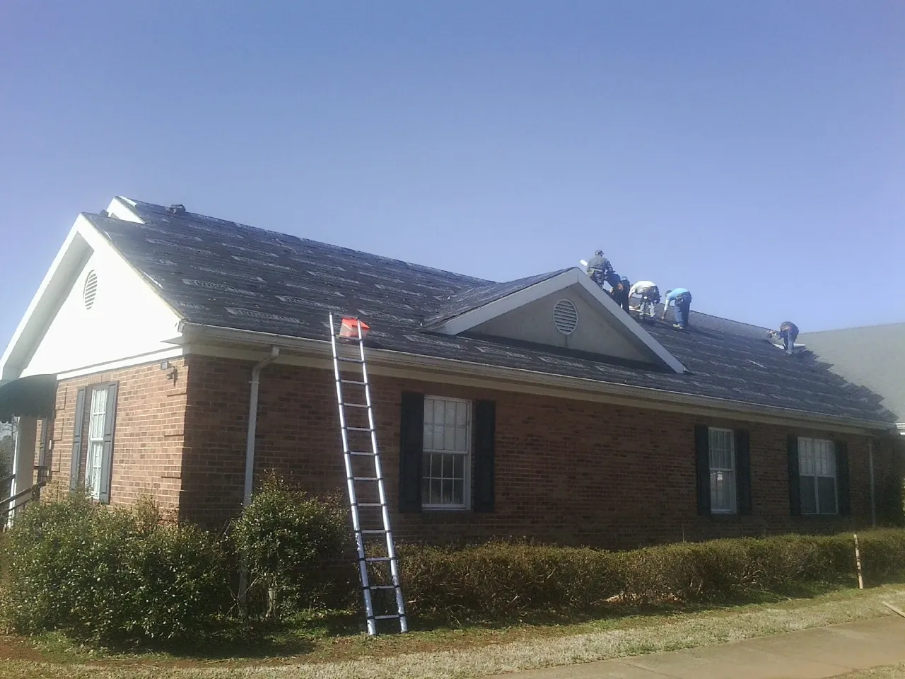 Crew tearing shingles off a brick ranch roof with a ladder set — Emergency Roof Repair work by our crew in Fall Branch