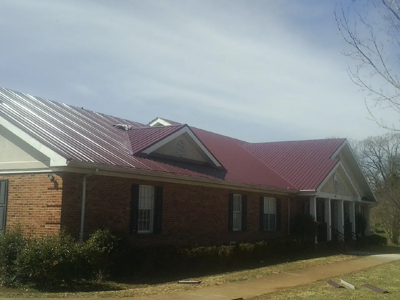 Red metal roof with gabled entries on a long brick building, from a Hail Damage Roof Repair job in Fall Branch