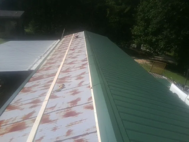 Old rusted panels beside newly installed green metal roofing — Wind Damage Roof Repair by Roofing Brothers in Fall Branch
