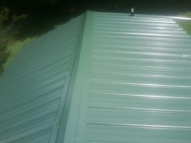 New green metal panels meeting at the ridge of a roof — Flat Roof Repair work by our crew in Fall Branch