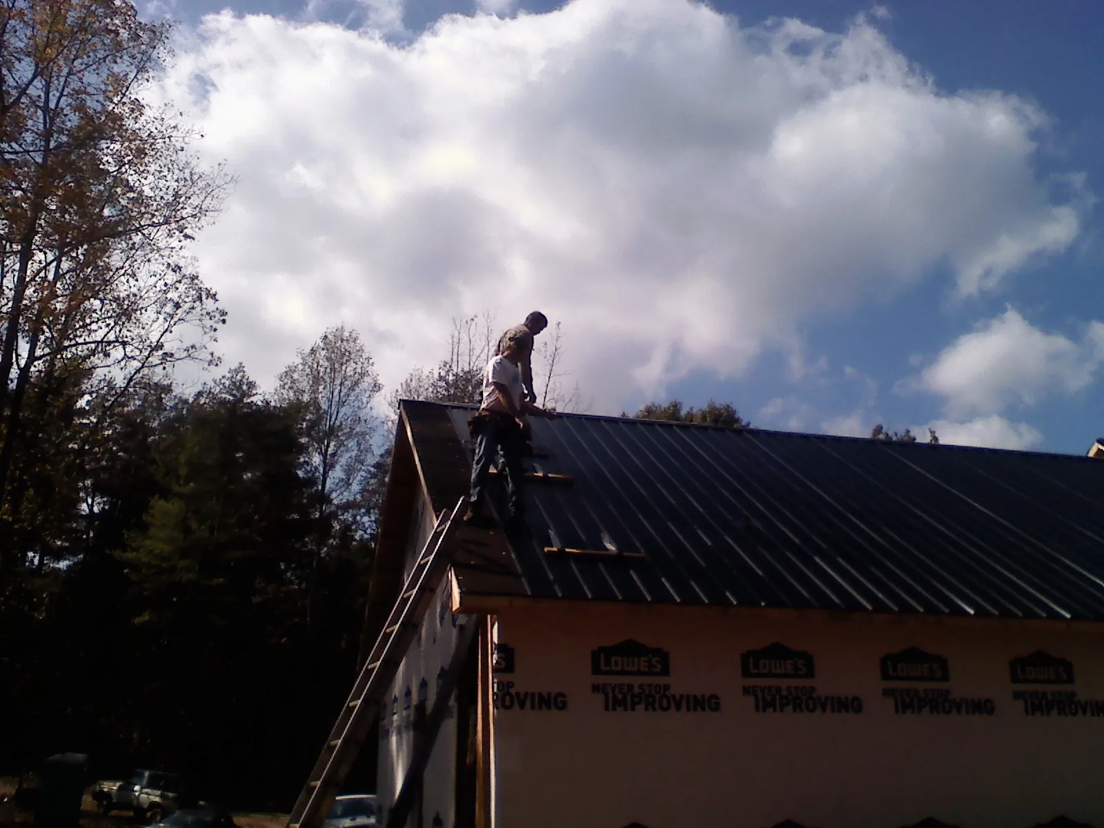 Roofer fastening dark metal panels high against a cloudy sky, from a Roof Inspection job in Fall Branch