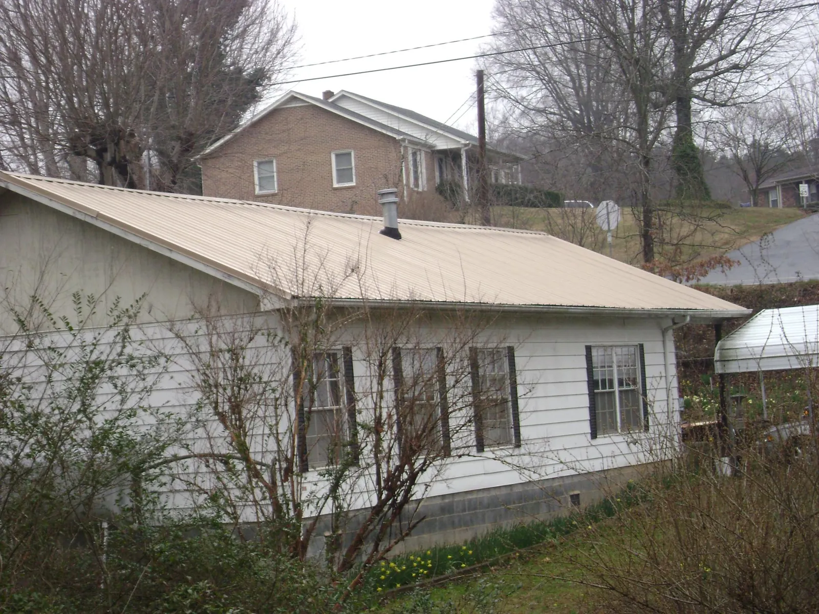 Tan metal roof on a white sided house set into a hillside — Commercial Roofing by Roofing Brothers in Fall Branch
